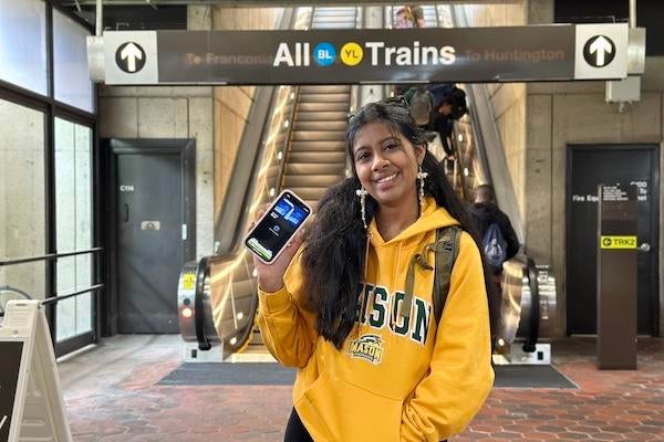 George Mason University student showing a mobile transit pass at a Metro station near the Blue and Yellow lines